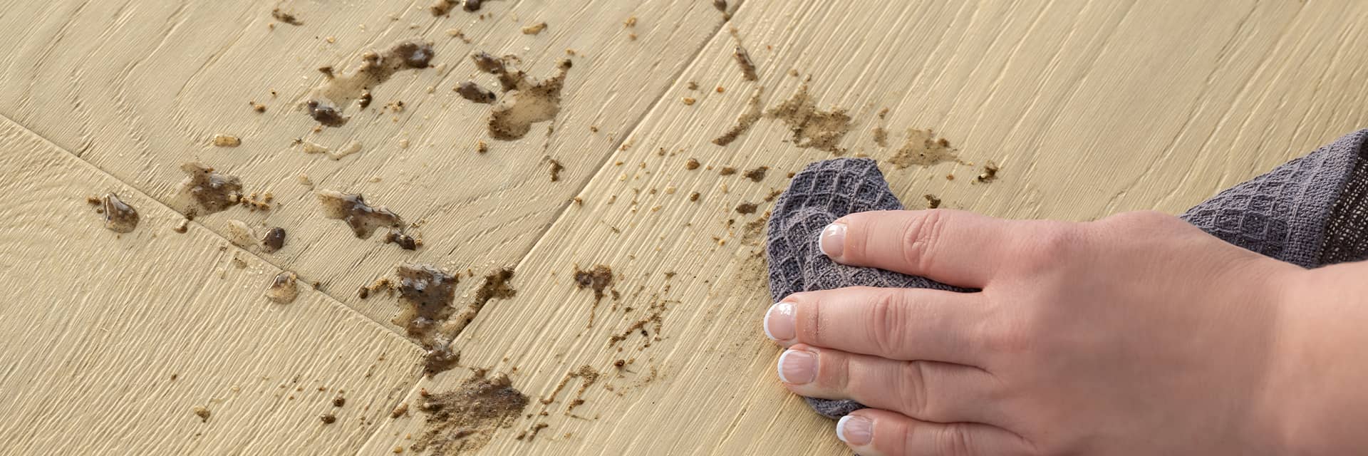 mujer limpiando barro de un suelo de madera noble beige con un paño de microfibra
